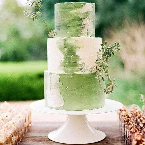 Three-tier wedding cake with leaf green and white luster dust frosting, adorned with greenery.