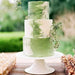 Three-tier wedding cake with leaf green and white luster dust frosting, adorned with greenery.