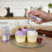 Three cupcakes being sprayed by a Liliac Purple color Edible Glitter 4 gram pump. | bakell.com