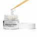 White edible shimmer flakes in a clear jar with a wooden tool sprinkling flakes.