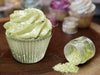 Neon green Tinker Dust edible glitter sprinkled on a cupcake next to an open jar.