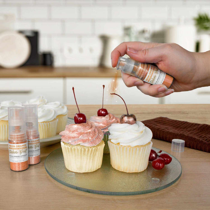 Three cupcakes being sprayed by a Neon Orange color Edible Glitter 4 gram pump. | bakell.com