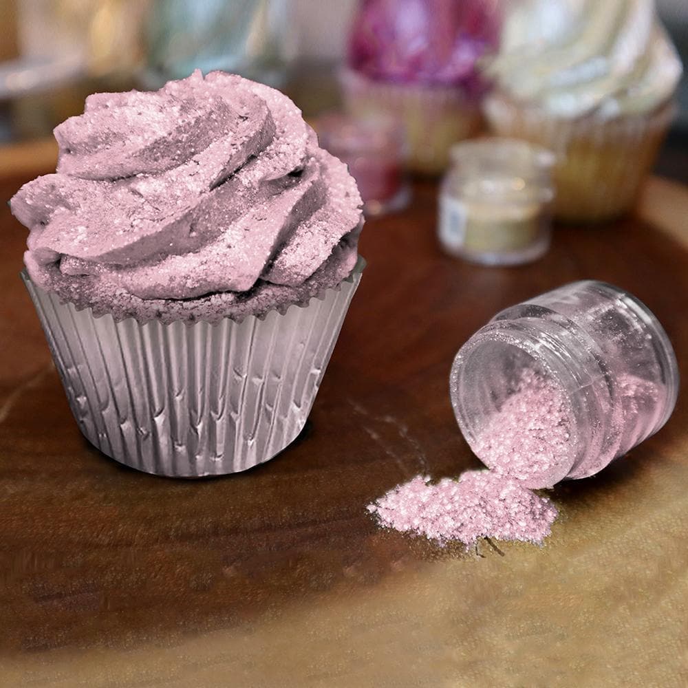 Pink Tinker Dust edible glitter on a cupcake and spilled from a jar on a wooden surface.
