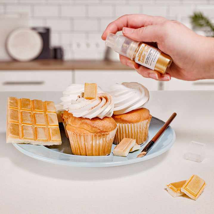 Three cupcakes and a wafer being sprayed by a Gold color Luster Dust 4 gram pump. | bakell.com