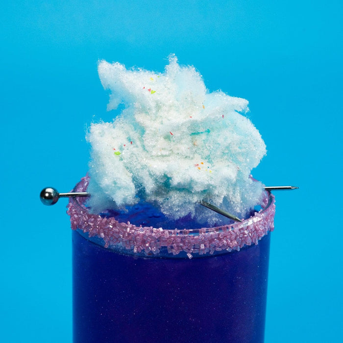 Purple drink with a pink sugar rim, topped with light blue cotton candy and colorful sprinkles.