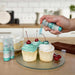 Three cupcakes being sprayed by a Turquoise color Edible Glitter 4 gram pump. | bakell.com