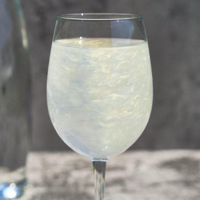 A clear wine glass filled with a shimmering, iridescent light-colored beverage.