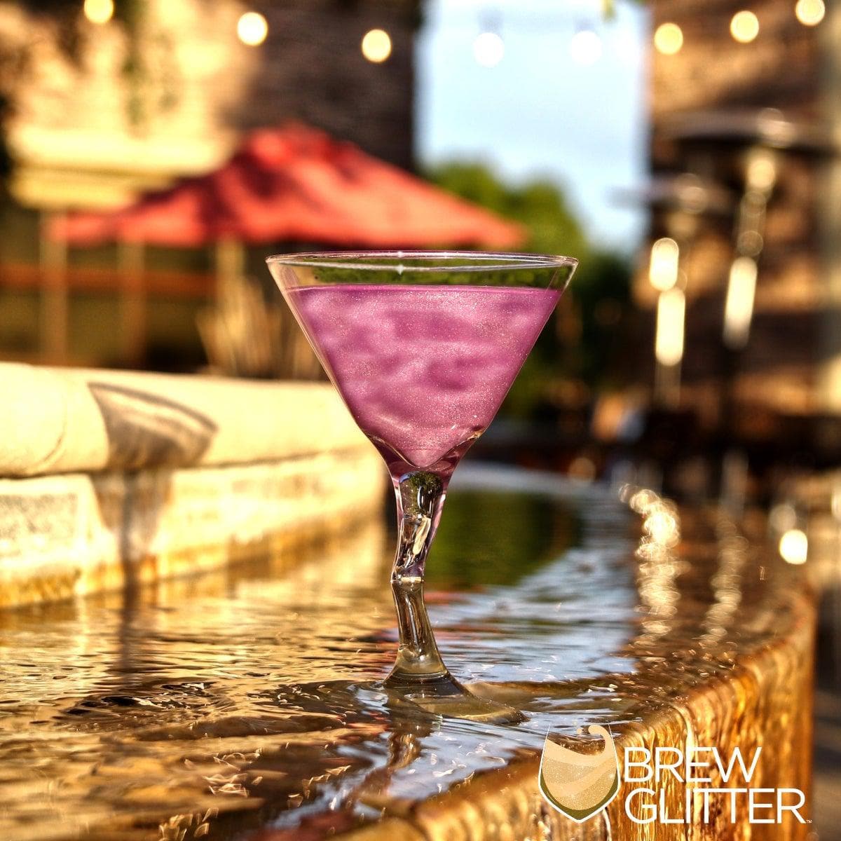 Purple iridescent edible glitter drink in a martini glass with a unique stem, on a wet stone surface.